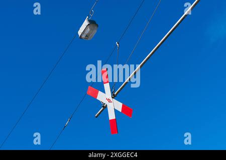 Un segnale rosso e bianco di attraversamento della ferrovia pende da un palo di metallo contro un cielo blu brillante. Foto Stock