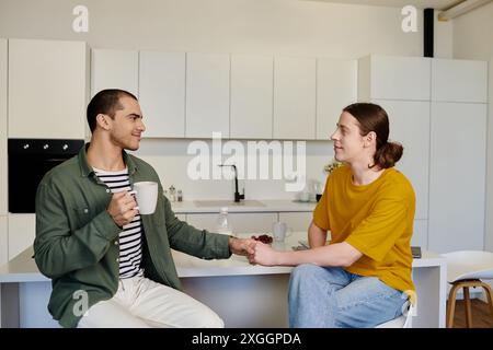 Una giovane coppia gay si gode un caffè mattutino insieme nella loro cucina moderna. Foto Stock