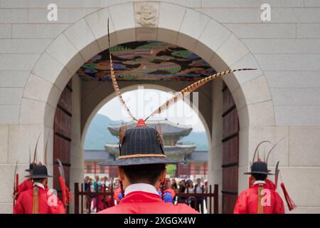 Le guardie coreane del palazzo con le tradizionali uniformi rosse e i cappelli decorati sono all'attenzione sotto una porta ad arco Foto Stock