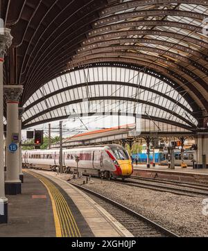 Lo storico arco curvo copre l'ingresso di una stazione ferroviaria e un treno entra alla banchina far. Le colonne sono in primo piano. Foto Stock