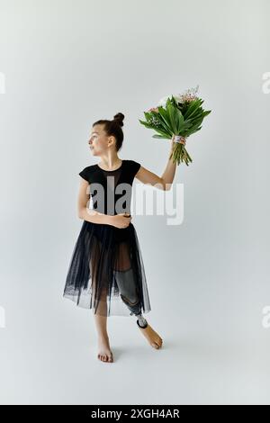 Una giovane ragazza con una gamba protesica posa con grazia in un filetto nero e una gonna in tulle, tenendo in mano un mazzo di fiori. Foto Stock