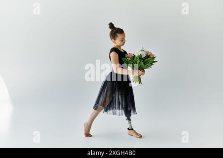 Una giovane ragazza con una gamba protesica posa in uno studio di ginnastica, tenendo in mano un mazzo di fiori. Foto Stock