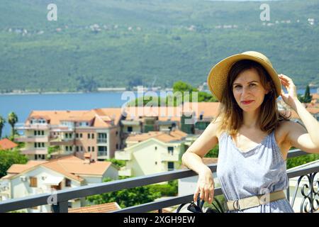 Ritratto di una turista donna venuta in vacanza sulla costa del Montenegro. Una donna sorridente con un cappello si erge su un balcone Foto Stock