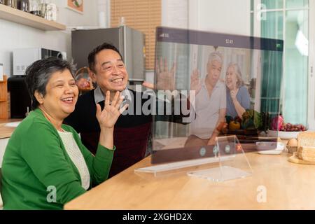 Uomo e donna dai capelli grigi che videochiama i parenti usando un laptop, abbracciandosi, seduti a un tavolo, comunicando con amici anziani. comunicazione virtuale si Foto Stock