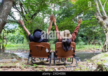 Vista posteriore di una giovane coppia seduta nella loro splendida natura. Coppia seduta su una sedia tenendosi per mano e godendo di una splendida vista sulle montagne Foto Stock