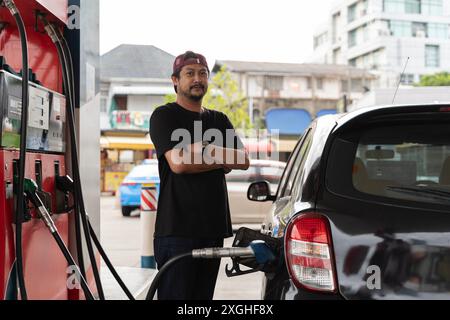 Ritratto di un uomo d'affari sorridente che rifornisce la sua auto di lusso al distributore di benzina. Manuale conducente rabbocco e pompaggio a mano dell'olio di benzina della vettura con carburante a. Foto Stock