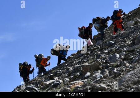 (240709) -- AKTO, 9 luglio 2024 (Xinhua) -- Taxibayi Janibaiki (2° L) marcia in salita sulle pendici di Muztagh Ata, trasportando circa 25 chilogrammi di attrezzature a fianco dei suoi compagni nella regione autonoma Xinjiang Uygur della Cina nord-occidentale, 4 luglio 2024. Il Muztagh Ata, situato sull'altopiano di Pamir a un'altitudine di oltre 7.500 metri nella regione autonoma di Xinjiang Uygur, nella Cina nord-occidentale, è un'attrazione per gli appassionati di alpinismo provenienti da tutto il mondo. Durante la stagione delle arrampicate, la gente si riunisce nel villaggio di Subax, nella contea di Akto, ai piedi del Muztagh Ata per l'alpinismo. Per quanto riguarda quelli Foto Stock