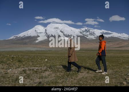 (240709) -- AKTO, 9 luglio 2024 (Xinhua) -- Taxibayi Janibaiki (R) e suo padre Janibaiki Burunbayi camminano su un pascolo ai piedi di Muztagh Ata nella regione autonoma dello Xinjiang Uygur, nella Cina nord-occidentale, 6 luglio 2024. Il Muztagh Ata, situato sull'altopiano di Pamir a un'altitudine di oltre 7.500 metri nella regione autonoma di Xinjiang Uygur, nella Cina nord-occidentale, è un'attrazione per gli appassionati di alpinismo provenienti da tutto il mondo. Durante la stagione delle arrampicate, la gente si riunisce nel villaggio di Subax, nella contea di Akto, ai piedi del Muztagh Ata per l'alpinismo. Per quanto riguarda la gente del posto che ha familiarità con la ter Foto Stock