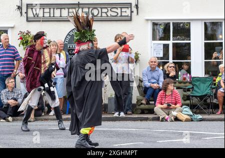 I Rendham Mummers celebrano il solstizio d'estate con la tradizionale vernice per il viso, 2018 e la strada fuori dal pub White Horse con traffico di passaggio. Foto Stock