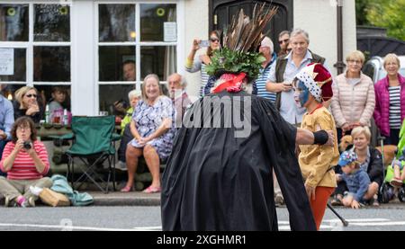 I Rendham Mummers celebrano il solstizio d'estate con la tradizionale vernice per il viso, 2018 e la strada fuori dal pub White Horse con traffico di passaggio. Foto Stock