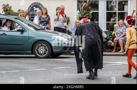 I Rendham Mummers celebrano il solstizio d'estate con la tradizionale vernice per il viso, 2018 e la strada fuori dal pub White Horse con traffico di passaggio. Foto Stock