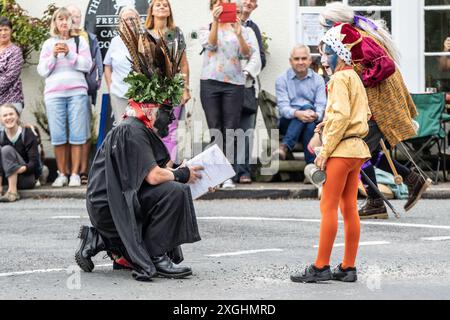 I Rendham Mummers celebrano il solstizio d'estate con la tradizionale vernice per il viso, 2018 e la strada fuori dal pub White Horse con traffico di passaggio. Foto Stock