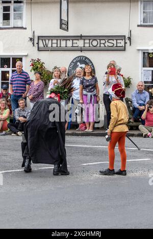 I Rendham Mummers celebrano il solstizio d'estate con la tradizionale vernice per il viso, 2018 e la strada fuori dal pub White Horse con traffico di passaggio. Foto Stock