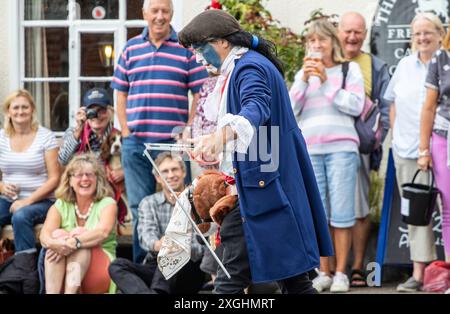 I Rendham Mummers celebrano il solstizio d'estate con la tradizionale vernice per il viso, 2018 e la strada fuori dal pub White Horse con traffico di passaggio. Foto Stock