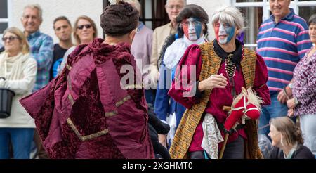 I Rendham Mummers celebrano il solstizio d'estate con la tradizionale vernice per il viso, 2018 e la strada fuori dal pub White Horse con traffico di passaggio. Foto Stock