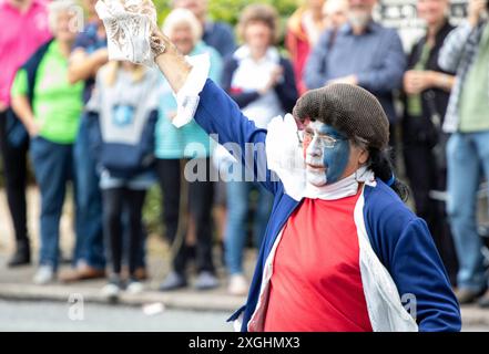 I Rendham Mummers celebrano il solstizio d'estate con la tradizionale vernice per il viso, 2018 e la strada fuori dal pub White Horse con traffico di passaggio. Foto Stock