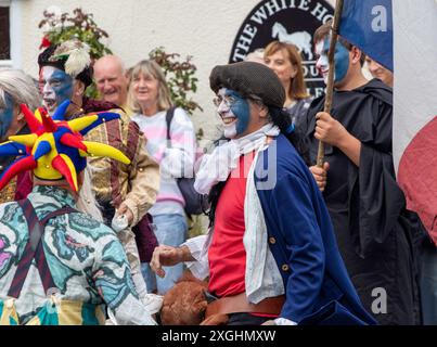 I Rendham Mummers celebrano il solstizio d'estate con la tradizionale vernice per il viso, 2018 e la strada fuori dal pub White Horse con traffico di passaggio. Foto Stock