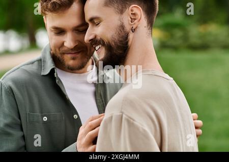 Una coppia gay barbuta condivide un momento tenero in un parco verde, con gli occhi chiusi in uno sguardo pieno di affetto. Foto Stock