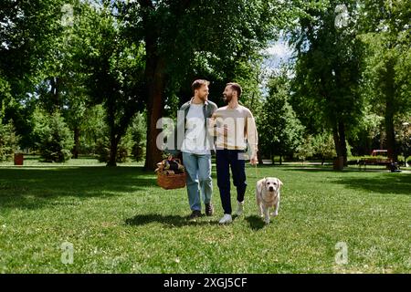 Una coppia gay barbuta cammina mano nella mano attraverso un parco verde con il loro Labrador retriever, godendosi un pomeriggio di sole. Foto Stock