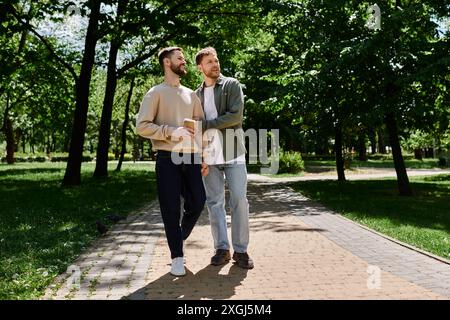 Due uomini barbuti, vestiti in modo informale, si tengono per mano e attraversano un parco in una giornata di sole. Foto Stock