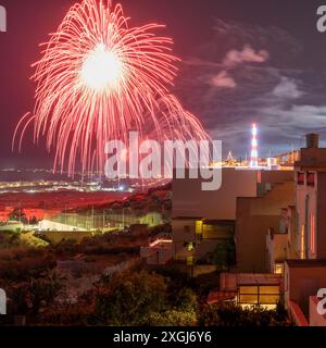 I meravigliosi fuochi d'artificio rossi illuminano il cielo notturno su un paesaggio urbano, creando un'atmosfera vivace e festosa. Perfetto per i festeggiamenti. Foto Stock