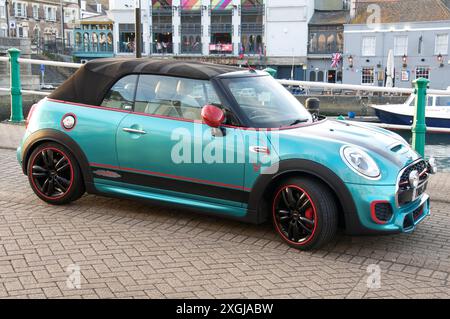 Un'auto a motore convertibile personalizzata Mini Cooper F57 turchese, parcheggiata sul lungomare di Weymouth Harbour. Dorset, costa meridionale, Inghilterra, Regno Unito, Gran Bretagna. Foto Stock