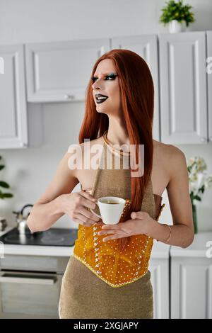 Una diva drag si diverte con una tazza di caffè indossando un elegante outfit dorato. Foto Stock