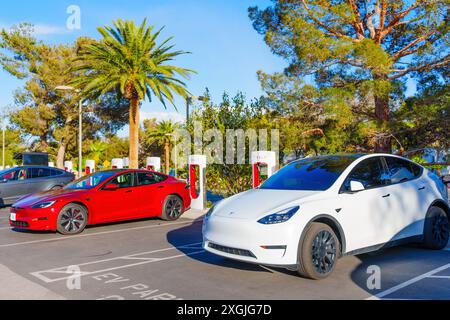 Los Angeles, California - 15 aprile 2024: Due auto elettriche, tra cui i modelli Tesla rossi e bianchi, si ricaricano presso la stazione Supercharger di Tesla su una S trasparente Foto Stock