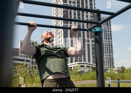 Il bel barbuto fa i tiri sul bar orizzontale in strada sul campo sportivo. All'aperto. Estate. Allenamento. Routine mattutina. Foto Stock