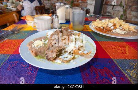 Delizioso piatto messicano con tenera costoletta di manzo, fagioli fritti e tortillas fresche. La tovaglia vivida mette in risalto l'atmosfera rustica, perfetta per un culto Foto Stock