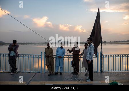 I musulmani sciiti del Kashmir osservano l'alta bandiera religiosa eretta su una strada durante Muharram. Muharram iniziò in Kashmir con profonda riverenza, specialmente tra la comunità musulmana sciita, commemorando il martirio dell'imam Hussain nella battaglia di Karbala. I primi dieci giorni, che culminano con l'Ashura, presentano processioni solenni in cui i lori vestiti di nero portano striscioni e eseguono ritmici battendo il petto. Si tengono raduni Majlis dove gli studiosi religiosi raccontano gli eventi di Karbala, e le recitazioni emotive di Marsiya sono comuni. Intricati standard Taziyah e Alam, simboleggiano l'IS Foto Stock