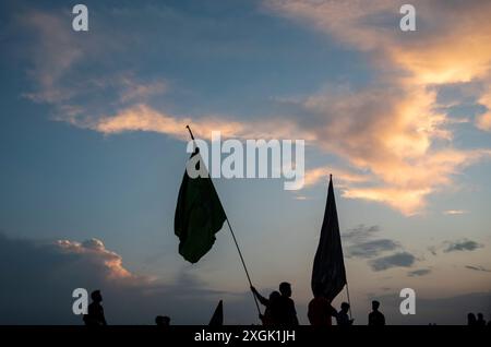 Silhouette di musulmani sciiti del Kashmir che tengono bandiere religiose su una strada durante Muharram. Muharram iniziò in Kashmir con profonda riverenza, specialmente tra la comunità musulmana sciita, commemorando il martirio dell'imam Hussain nella battaglia di Karbala. I primi dieci giorni, che culminano con l'Ashura, presentano processioni solenni in cui i lori vestiti di nero portano striscioni e eseguono ritmici battendo il petto. Si tengono raduni Majlis dove gli studiosi religiosi raccontano gli eventi di Karbala, e le recitazioni emotive di Marsiya sono comuni. Intricati standard Taziyah e Alam, simboleggiano l'IS Foto Stock