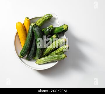 Vista dall'alto di una ciotola bianca piena di zucchine fresche, che presenta un mix di varietà verdi e gialle. La disposizione evidenzia i colori vivaci di un Foto Stock