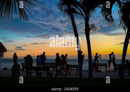 La gente si riunisce al tramonto per una festa in spiaggia sotto le palme dei Caraibi Foto Stock