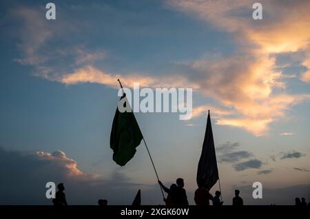 Silhouette di musulmani sciiti del Kashmir che tengono bandiere religiose su una strada durante Muharram. Muharram iniziò in Kashmir con profonda riverenza, specialmente tra la comunità musulmana sciita, commemorando il martirio dell'imam Hussain nella battaglia di Karbala. I primi dieci giorni, che culminano con l'Ashura, presentano processioni solenni in cui i lori vestiti di nero portano striscioni e eseguono ritmici battendo il petto. Si tengono raduni Majlis dove gli studiosi religiosi raccontano gli eventi di Karbala, e le recitazioni emotive di Marsiya sono comuni. Intricati standard Taziyah e Alam, simboleggiano l'IS Foto Stock