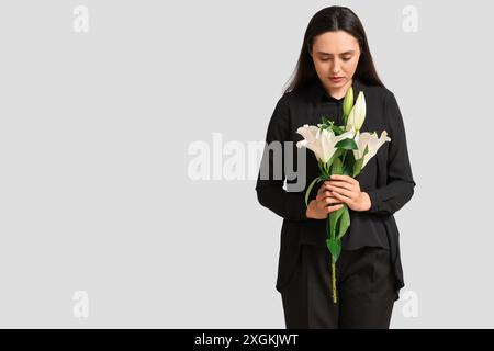 Giovane donna con bouquet funebre di fiori di giglio su sfondo bianco Foto Stock