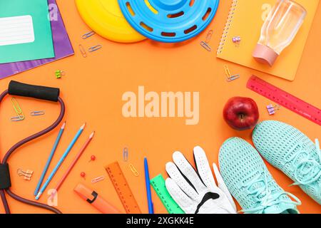 Telaio realizzato con sneakers, frisbee, mela, espansore e diversi articoli di cancelleria su sfondo arancione Foto Stock