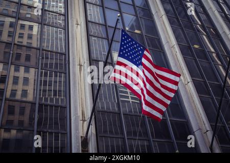 Bandiera americana che sventola di fronte a un moderno grattacielo di vetro a New York; simbolo nazionale degli Stati Uniti con riflessi dell'architettura urbana a Manhattan, Stati Uniti Foto Stock