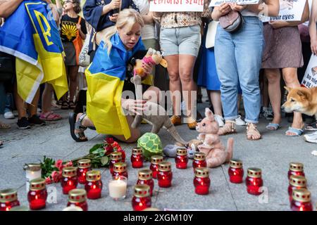 Una donna avvolta nella bandiera Ucraina posiziona giocattoli in onore dei bambini morti nell'attacco all'ospedale infantile di Kiev durante la manifestazione. Il 9 luglio, il giorno dopo il bombardamento russo dell'ospedale pediatrico di Okhmatdyt, diverse centinaia di persone si sono riunite per protestare contro gli attacchi agli ospedali in Ucraina. Nei loro discorsi, i manifestanti hanno confermato che si trattava di un missile russo e non - come sostiene la propaganda russa - di un missile antiaereo ucraino. Nei loro discorsi, i manifestanti hanno anche chiesto alla NATO di chiudere il cielo sull'Ucraina e alle Nazioni Unite di fare di più invece Foto Stock