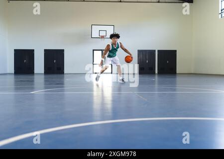 Un giovane uomo birazziale abbraccia sia lo sport che lo stile di vita mentre gioca a basket in casa. Si concentra sul gioco, facendo dribbling sul campo Foto Stock