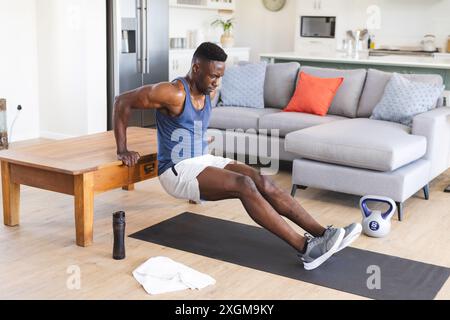 Adatta un uomo afroamericano che lavora a casa, facendo push up usando il tavolino da caffè. Fitness, allenamento, esercizio, vita domestica e stile di vita sano, una Foto Stock