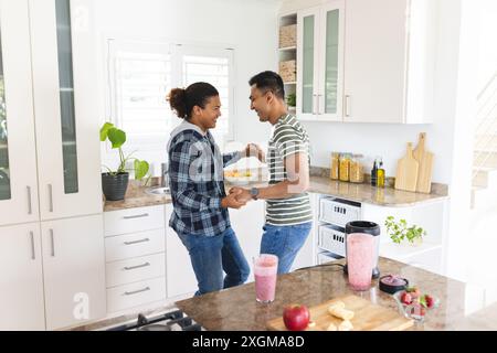 La coppia birazziale gay ama cucinare insieme a casa. Condividono un momento divertente in una cucina luminosa e moderna. Foto Stock