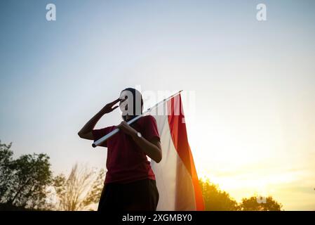 Ritratto di una donna che regge una bandiera indonesiana con un gesto rispettoso all'aperto con sfondo cielo all'alba Foto Stock