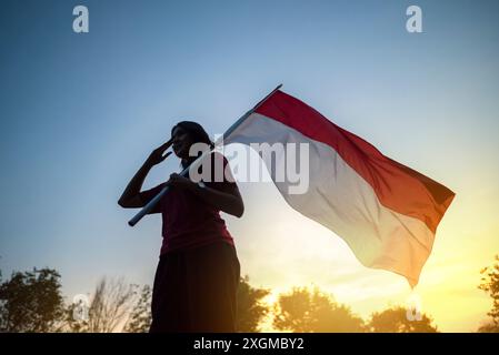 Ritratto di una donna che regge una bandiera indonesiana con un gesto rispettoso all'aperto con sfondo cielo all'alba Foto Stock