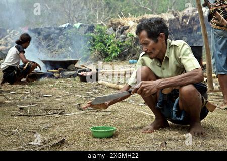 Un uomo pulisce il suo machete dopo aver dato una mano a fette di carne durante la preparazione di una festa relativa alla costruzione di case e ai rituali di inaugurazione a Ratenggaro, un villaggio indigeno situato a Umbu Ngedo, Kodi Bangedo, sudovest Sumba, East Nusa Tenggara, Indonesia. Attraverso una riunione dell'Assemblea generale nel dicembre 2023, le Nazioni Unite (ONU) hanno espresso un riconoscimento al "valore e alla diversità delle culture e della forma di organizzazione sociale dei popoli indigeni e alla loro conoscenza olistica e tradizionale delle loro terre, delle risorse naturali e dell'ambiente". Foto Stock