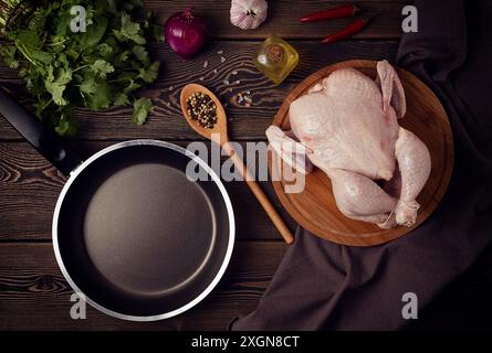 Pollo fresco crudo, spezie ed erbe aromatiche, padella, su un tavolo di legno, vista dall'alto, niente persone, tonificato Foto Stock