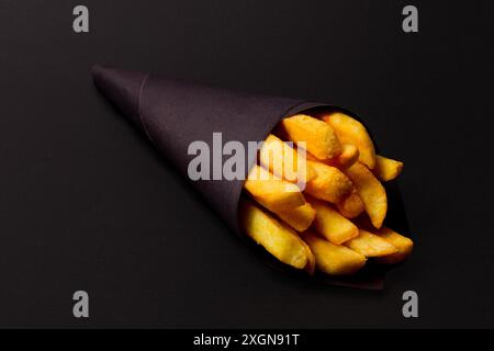 Patatine fritte, confezionate in carta nera, su sfondo nero, primo piano, selettivo Foto Stock