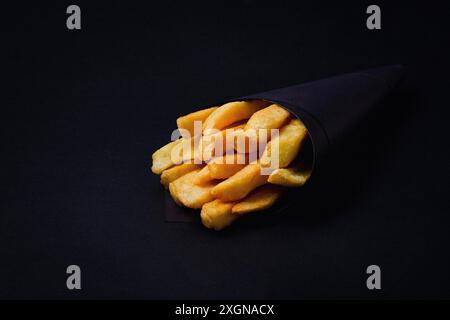 Patatine fritte, confezionate in carta nera, su sfondo nero, primo piano, selettivo Foto Stock