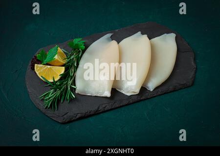 Corpo di calamaro fresco, crudo, tre carcasse, vista dall'alto, su ardesia nera, niente persone Foto Stock