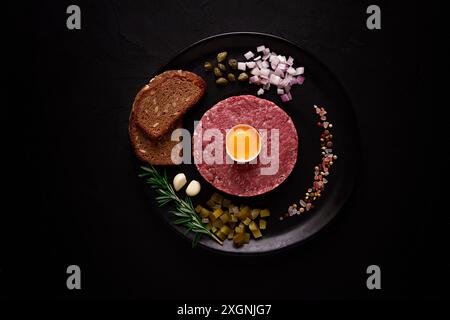 Tartare di manzo, con uova, capperi, cetriolini e pane, su sfondo nero, vista dall'alto, primo piano, orizzontale, nessuna persona Foto Stock